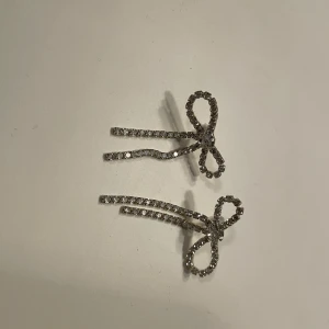 Glittriga rosettörhängen med stenar - Säljer ett par örhängen i form av rosetter, täckta med små gnistrande stenar. Örhängena är silvriga och har en elegant, lekfull design som verkligen drar blickarna till sig. Perfekta för dig som gillar accessoarer med det lilla extra.