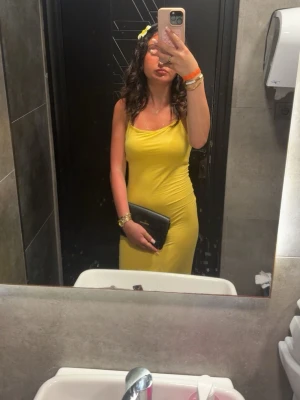 Gul figurnära långklänning - Snygg gul långklänning med smala axelband och figurnära passform. Klänningen har en enkel och stilren design som framhäver siluetten. Perfekt för sommarens alla tillfällen.