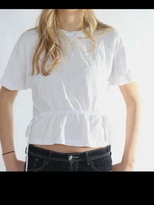 Vit croppad topp med volang - Säljer en vit croppad topp med korta ärmar och volang nedtill. Toppen har en avslappnad passform och resår i midjan som ger en snygg siluett. Perfekt till jeans eller kjol för en fräsch look.