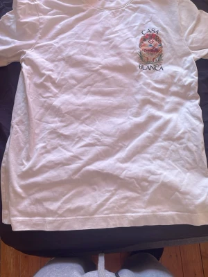 Vit t-shirt från Casablanca - Säljer en vit t-shirt från Casablanca med tryckt logga och motiv på bröstet. Klassisk rund hals och korta ärmar. Perfekt basic-plagg med snygg detalj framtill. Tillverkad i mjuk bomull för skön känsla. Pris kan diskuteras 