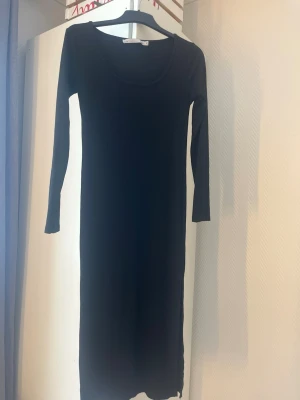 Svart ribbad långklänning 157 - Svart långklänning från 157 i ribbad bomullsmix. Klänningen har lång ärm och rund halsringning, perfekt för en enkel och stilren look. Passformen är normal och materialet känns mjukt mot huden.