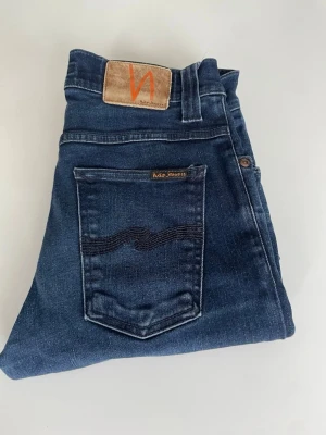Blå Nudie jeans - Säljer dessa sjukt snygga mörkblå nudie jeansen!  Den har en väldigt snygg mörkblå färg som passar till nästintill allt! Det är modell Grim Tim de motsvarar slim! På lappen står 28/34 men det är egentligen närmare w25 (34cm). Hör av dig vid frågor, pris är ej hugget i sten!