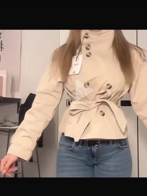 Beige trenchcoat med knytband - Stilren beige trenchcoat med hög krage, stora knappar och knytband i midjan. Jackan har en kortare, boxig passform och långa ärmar. Perfekt för dig som vill ha en trendig och klassisk look. Materialet ser ut att vara bomull eller en bomullsblandning.
