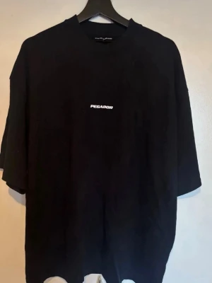 Svart t-shirt Pegador - Svart  t-shirt från Pegador med enkel vit logga på bröstet. T-shirten har rund hals och korta ärmar, perfekt för en avslappnad och trendig stil. 