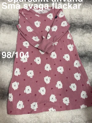 Rosa nattlinne med hundmotiv 98/104 - Sött rosa nattlinne med långa ärmar och gulligt mönster av vita hundar och små hjärtan. perfekt för mysiga kvällar hemma. Avslappnad passform och rund halsringning.🌸 Sparsamt använd. Små svaga fläckar. Storlek 98/104 