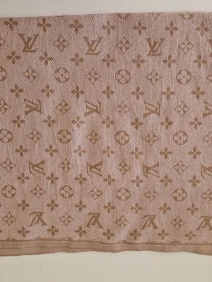 Ljusrosa Louis Vuitton sjal med monogram - Säljer en beige sjal från Louis Vuitton med det klassiska monogrammönstret i en ljusare beige ton. Sval och lyxig känsla, vävd i ett mjukt material med fransad kant på ena sidan. Perfekt accessoar för att lyfta vilken outfit som helst.