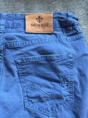 Blå jeans från Morris - Snygga blå jeans från Morris med klassisk femficksdesign och läderpatch bak i midjan. Jeansen har raka ben och är tillverkade i ett mjukt bomullsmaterial som ger en skön känsla. Perfekta för dig som vill ha en stilren och avslappnad look.