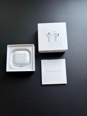 Apple AirPods 4 med faktura  - Säljer ett par vita Apple AirPods med tillhörande laddningsetui. Trådlösa hörlurar med stilren och kompakt design i plast. Perfekta för musik, samtal och träning. Levereras i originalförpackning med tillbehör.