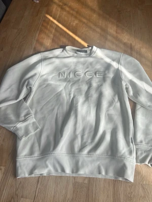 Biege sweatshirt från NICCE - Säljer en stilren beige sweatshirt från NICCE med broderad logga framtill. Tröjan har rund halsringning, långa ärmar och ribbade muddar. Perfekt för dig som gillar enkel och clean streetwear.
