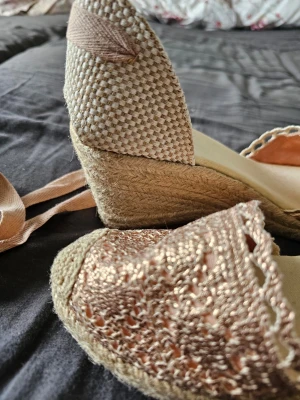 Rand BE Espadrillos / Kilklackar – Helt nya (Strl 41) 🌸✨ - Skick: Helt nya, aldrig använda och i absolut nyskick.Stl.: 41 (normala i storleken).Klackhöjd: Stabil och väldigt bekväm kilklack på ca 8 cm baktill samt en platå fram på ca 2 cm.Skorna har en vacker virkad spets i guldrosa/rosé över tån, en snyggt lite öppen baksida vid hälen och långa matchande band som knyts elegant runt vristen.✨ Missa inte mina andra annonser! ✨Jag rensar garderoben och säljer just nu flera unika rariteter och märkesartiklar. Perfekt för dig som vill hitta unika plagg !