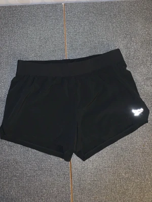 Svarta träningsshorts - Snygga svarta träningsshorts med bred resår i midjan och diskret logga på ena benet. Perfekta för gymmet eller löprundan, med en enkel och sportig design som passar till det mesta.