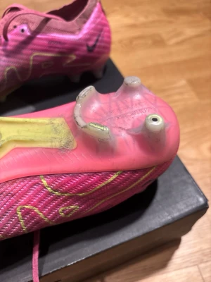 Nike Air Zoom Mercurial - Säljer ett par kraftfulla Nike Air Zoom Mercurial i en iögonfallande rosa färgställning. Dessa skor är byggda för explosiv fart och precision på planen – ett perfekt val för den seriösa spelaren. 