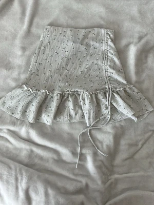 Blommig volangkjol från Gina Tricot - Supersöt kortkjol från Gina Tricot i ljus färg med små blommor och volangkant. Kjolen har snörning på sidan och är gjord i ett mjukt, ribbat material. Perfekt för dig som vill ha en feminin och trendig look. Priset kan diskuteras!