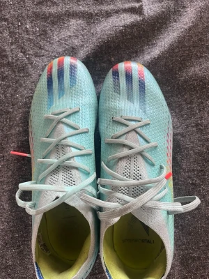 Adidas X speedpoortal Turkosa fotbollsskor med färgglada detaljer - Säljer ett par snygga turkosa fotbollsskor med snörning och lågt skaft från adidas . Skorna har färgglada detaljer i blått, rött och gult på ovandelen samt bl en ventilerande meshstruktur. Perfekta för dig som vill sticka ut på planen!