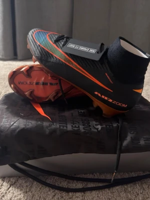 Elite Nike Air Zoom Mercurial fotbollsskor - Säljer ett par Nike Air Zoom Mercurial fotbollsskor med Dynamic Fit Boot. Skorna är svarta med orange detaljer och har en hög strumpkrage för extra stöd. Yttersulan är orange och skon har en modern, aerodynamisk design perfekt för snabba spelare på planen. Och skorna är Limited edition. Köpte dom helt nya men dom passa de mig inte. Storlek 42.5 pris kan diskuteras!