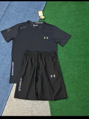 Svart träningsset från Under Armour - Snyggt svart träningsset med t-shirt och shorts från Under Armour. Båda plaggen har logga och text i regnbågsfärger. T-shirten har rund hals och kort ärm, shortsen har resår i midjan. Perfekt för gym eller löpning.