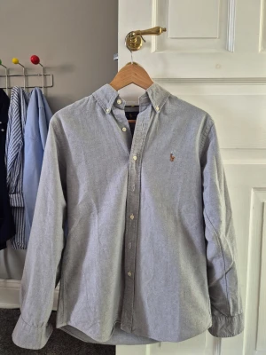 Grå skjorta från ralph lauren  [pris kan diskuteras] - Klassisk ljusblå skjorta med button-down krage och broderad logga på bröstet. Skjortan har långa ärmar och vita knappar framtill. Tillverkad i bomull för en skön och avslappnad känsla.