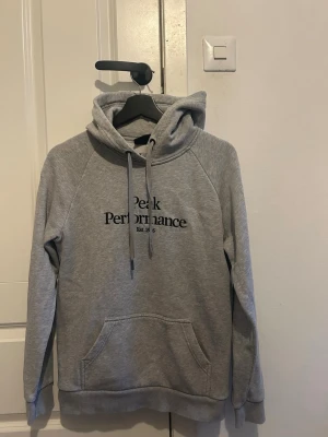 Grå hoodie Peak Performance - Snygg grå hoodie från Peak Performance med svart broderad logga på bröstet. Skriv till mig om funderingar och pris!!