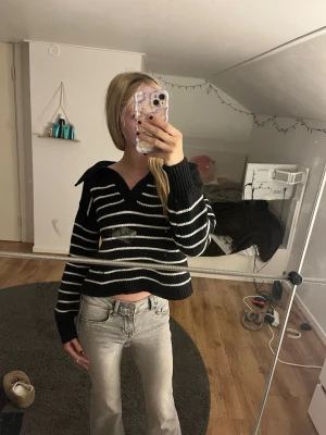 Svartvitrandig croppad stickad tröja - Trendig croppad stickad tröja i svart och vitt med breda ränder och v-ringad krage. Tröjan har långa ärmar och ribbade muddar. Perfekt för dig som gillar en avslappnad men snygg stil.