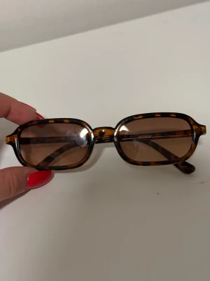 Bruna rektangulära solglasögon Bik Bok  - Snygga solglasögon med rektangulära bågar i brunsköldpaddsmönster och bruna glas. Klassisk och trendig look som passar till många stilar. Bågarna är i plast och har en cool vintagevibe.