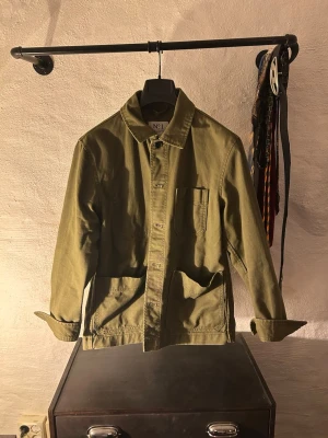 Olivgrön overshirt med fickor - Stilren olivgrön overshirt i bomull med klassisk krage, knappstängning och tre fickor framtill. Perfekt lager på lager-plagg med avslappnad passform och uppvikta ärmar för en casual look.