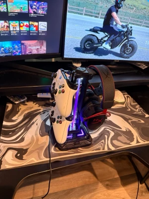 Gamingställ för kontroller och headset - Snyggt gamingställ med LED-belysning för att organisera två spelkontroller och ett headset. Stället är svart med blått ljus och har plats för både Xbox- och Playstation-kontroller samt gamingheadset. Perfekt för att hålla skrivbordet prydligt och gamingprylarna samlade.