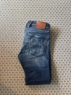 Blå slim fit jeans från replay - Säljer ett par blå slim fit jeans med snygga slitningar och kontrastsömmar. 