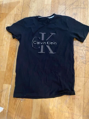 Svart Calvin Klein t-shirt - Snygg svart t-shirt från Calvin Klein med stort CK-logotyptryck på bröstet i vitt. Klassisk passform och rund halsringning. Perfekt till jeans eller shorts för en clean och stilren look.