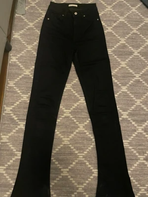 Svarta utsvängda jeans - Säljer ett par svarta jeans med hög midja och utsvängda ben. Klassisk femficksmodell med knapp och dragkedja framtill. Snygga att styla med sneakers eller boots för en trendig look.