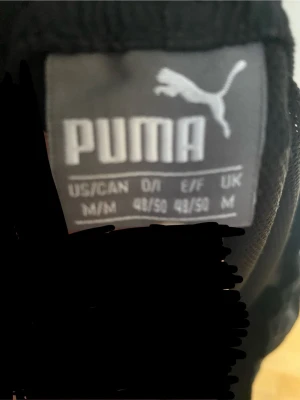 Svarta mjukisbyxor från Puma - Säljer ett par svarta mjukisbyxor från Puma med klassisk logga broderad på benet. Byxorna har en avslappnad passform och är perfekta för chill dagar. Tillverkade i mjukt material som känns skönt mot huden.