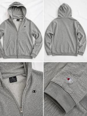 Grå zip hoodie från Champion - Snygg gråmelerad hoodie från Champion med dragkedja framtill och två fickor. Klassisk huva och ribbade muddar vid ärmar och nederkant. Champion-logga broderad på bröstet och ärmen. Mjuk insida i fleece för extra komfort.