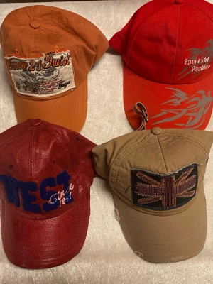 Fyra kepsar i olika färger och stilar - Fyra kepsar i olika färger: orange med broderad patch, röd med tryckt text och mönster, vinröd med blå text och broderi, samt beige med Union Jack-flagga i paljetter. Alla har böjd skärm och justerbar rem bak. Perfekta för dig som vill ha unika accessoarer. Helt ny 125kr/st