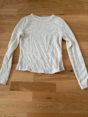 Vit stickad långärmad tröja - Säljer en tunnstickad vit tröja med lång ärm och rund halsringning. Tröjan har ett diskret mönster i stickningen och är lätt figursydd. Perfekt att styla med jeans eller kjol för en enkel och fräsch look. Lite genomskinlig 