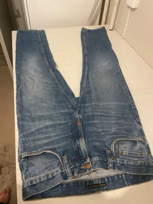 Nudie Jeans Gritty Jackson - Ett par klassiska blå jeans från Nudie Jeans med rak passform och fem fickor. Jeansen har snygga slitningar och kontrastsömmar, tillverkade i bomullsdenim. 