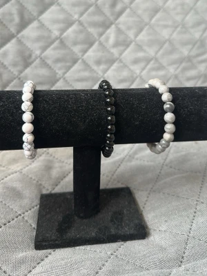 Set med tre pärlarmband - Säljer ett set med tre elastiska armband med pärlor. Ett armband har vita pärlor med grå marmorering, ett är helsvart med glansiga pärlor och det tredje har ljusgrå pärlor med subtil marmorering. Perfekt för dig som gillar stilrena accessoarer. 1 är 75kr, 2 är 130kr och alla 3 är 200kr.
