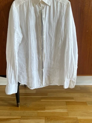 Vit linneskjorta från These Glory Days - Klassisk vit skjorta i 100% linne från These Glory Days. Skjortan har lång ärm, knappar framtill och en avslappnad passform. Perfekt till både jeans och chinos för en clean look. Endast använd cirka 3 gånger