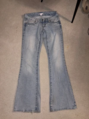 Ljusblå bootcut jeans med brodyr - Säljer ett par ljusblå bootcut jeans i klassisk denim med snygg brodyr på bakfickorna. Jeansen har fem fickor, bälteshällor och dragkedja med knapp. Perfekta för dig som gillar retrovibbar och vill ha ett par jeans med unik detalj.