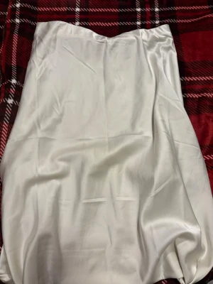 Vit satinkjol från Lager157 - Säljer en stilren vit långkjol i satin från Lager157. Kjolen har en mjuk och glansig yta som ger en lyxig känsla och passar perfekt till olika outfits. Enkel design utan synliga detaljer för en clean look.