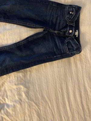 Mörkblå skinny jeans med kontrastsömmar - Säljer ett par mörkblå utsvängda jeans med vita kontrastsömmar och klassisk femficksdesign. Jeansen har låg midja och smal passform hela vägen ner. Perfekta till sneakers eller boots för en clean look.