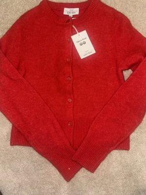 Röd kofta från & Other Stories - Kofta i klar röd färg från & Other Stories, tillverkad i alpackaull. Modellen har rund halsringning, knäppning framtill med matchande knappar och ribbade muddar vid ärmslut och nederkant. Perfekt för lager på lager och en färgklick i garderoben.