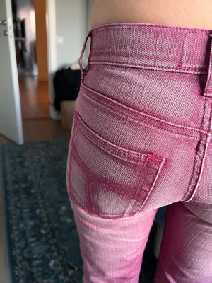  Låg midjade Rosa tiger of Sweden jeans🤩 - Säljer ett par unika rosa jeans med raka ben och tydliga kontrastsömmar. Jeansen har klassiska bakfickor och en svart patch bak i midjan. Materialet är denim med en cool tvättad effekt som ger en trendig look.