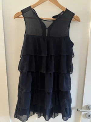 Mörkblå kort volangklänning  - Säljer en mörkblå kortklänning med flera lager volanger och transparent mesh upptill. Den saknar en knapp högst upp men är annars i bra skick💕