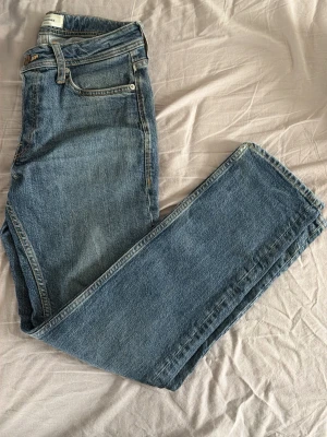 Blåa Jeans Från Jack And Jones Straight/Tim - Säljer ett par klassiska blå jeans från Jack And Jones med rak passform. Jeansen har fem fickor, bälteshällor och stängs med knapp. Tillverkade i slitstarkt denimtyg som ger en tidlös look. Endast 149kr, pris går att diskuteras.