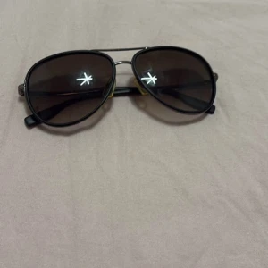 Svarta aviator-solglasögon Hugo Boss - Snygga svarta aviator-solglasögon från Hugo Boss med mörka glas och tunna metallbågar. Skalmarna har en cool textur och diskret logga på sidan. Klassisk modell som ger en stilren vibe och passar perfekt till sommaren. 100% äkta 