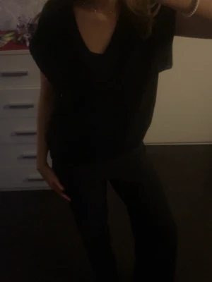 Svart v-ringad topp - En enkel svart topp med v-ringning och korta ärmar. Toppen har en lös passform och är perfekt för en avslappnad stil. Inga synliga mönster eller detaljer, vilket gör den lätt att matcha med olika outfits.