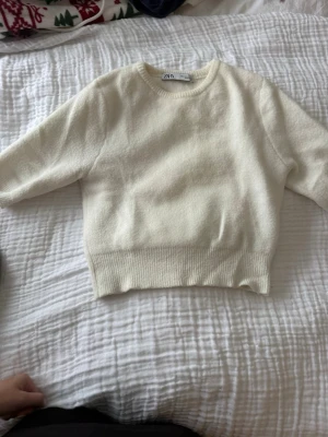Krämvit stickad tröja från Zara - Mysig krämvit stickad tröja från Zara med rund halsringning och ribbade muddar. Tröjan har en boxig passform och är tillverkad i ett mjukt material som känns skönt mot huden. Perfekt att matcha med jeans eller kjol.