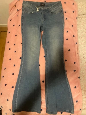 Blå bootcut jeans från Vero Moda - Snygga blå bootcut jeans från Vero Moda med låg midja och klassisk femficksdesign. Jeansen har en lätt tvättad look och utsvängda ben, perfekta för en trendig och avslappnad stil.