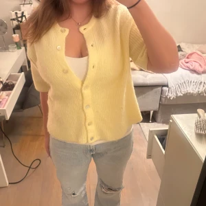 Gul stickad kofta med knappar - Superfin ljusgul stickad kofta med kort ärm och rund hals. Endast använd 1-2 gånger därav i princip nyskick!