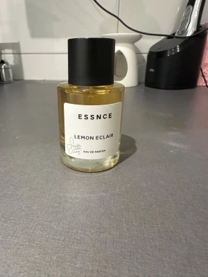 ESSNCE Lemon Eclair Eau de Parfum - Fräsch parfym från ESSNCE med doften Lemon Eclair. Flaskan är cylindrisk i genomskinligt glas med gul vätska och har en svart, matt kork. Stilig och enkel design med vit etikett framtill. Perfekt för dig som gillar citrusdofter. Helt oanvänd och aldrig provad 