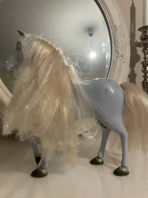 Ljusblå  leksakshäst med långt man - Säljer en ljusblå plastleksakshäst med långt, glittrigt blont man och svans. Hästen har gröna hovar och röda ögon. Perfekt som dekoration eller leksak för hästälskare.